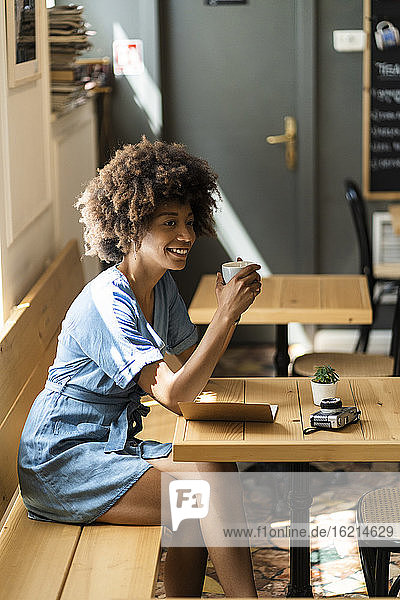 Nachdenkliche Frau  die eine Kaffeetasse hält  während sie am Tisch in einem Café sitzt
