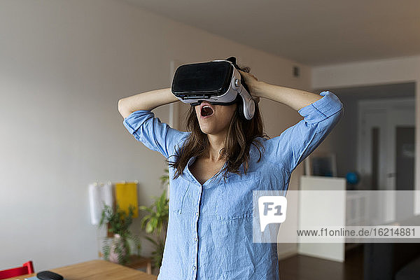 Junge Frau mit offenem Mund  die durch einen Virtual-Reality-Simulator schaut  während sie in ihrem Büro steht