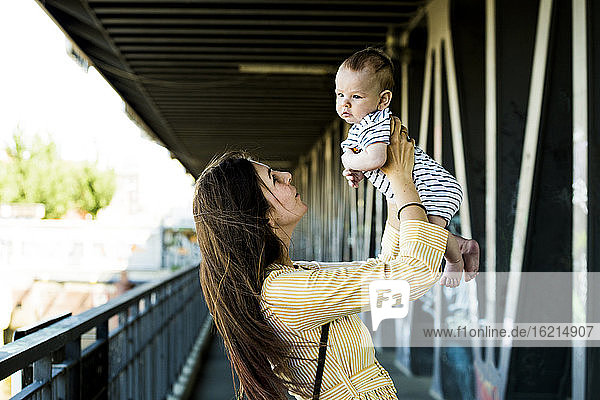 Mutter hebt ihren kleinen Jungen auf einer Brücke hoch