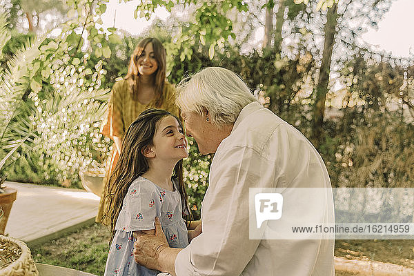 Smiling woman looking at girl playing with grandmother in yard