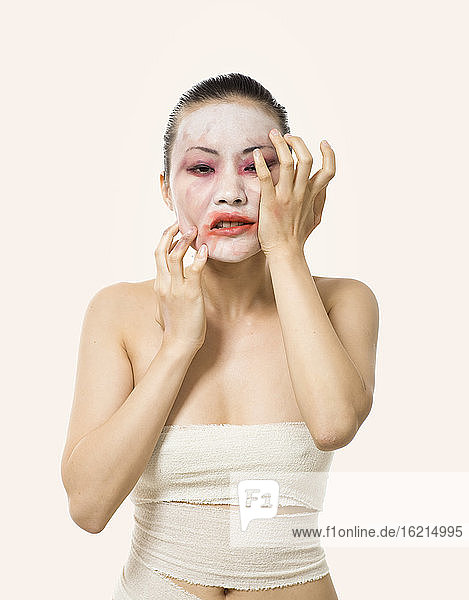 Nahaufnahme einer jungen Frau  die ihr Opern-Make-up verschmiert  während sie vor einem weißen Hintergrund steht