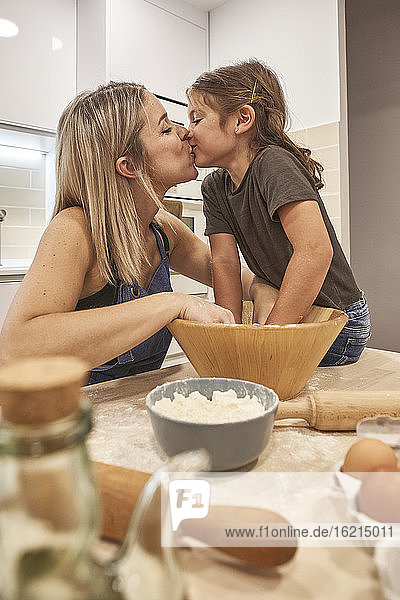 Verliebte Mutter und Tochter küssen sich beim Kneten von Pizzateig in der Küche
