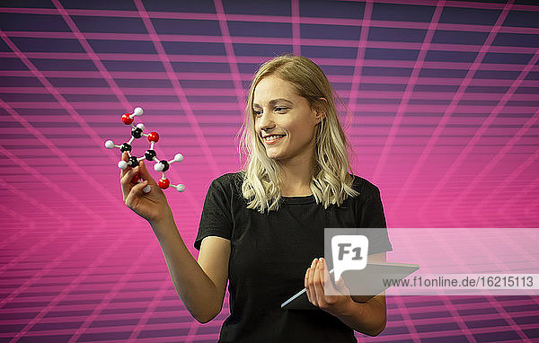 Wissenschaftlerin hält Molekülmodell und digitales Tablet  während sie vor einem Gittermuster steht