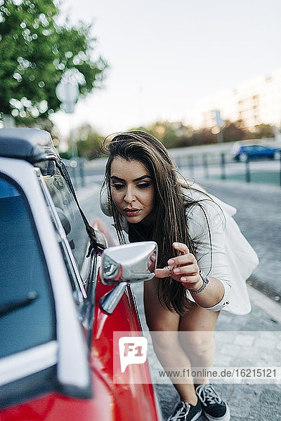 Young woman checking her look in mirror of car