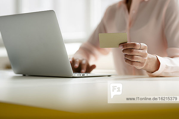 Nahaufnahme einer Geschäftsfrau  die eine Kreditkarte hält und einen Laptop am Schreibtisch im Büro benutzt