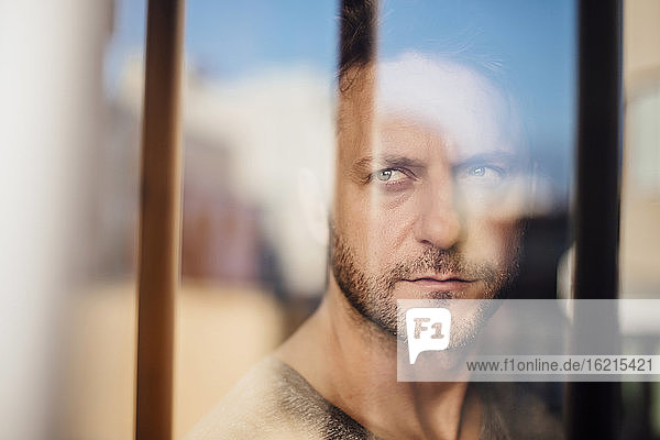 Nahaufnahme eines nachdenklichen Mannes,  der durch ein Fenster schaut,  gesehen durch Glas