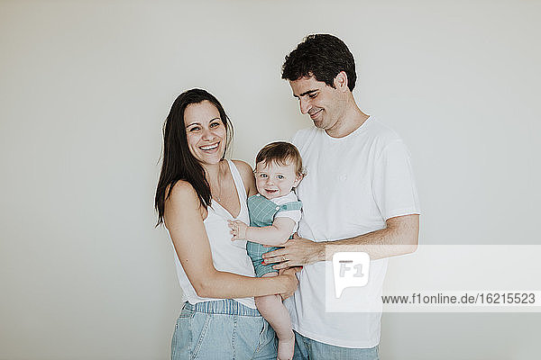 Cheerful parents carrying cute daughter while standing against white wall at home