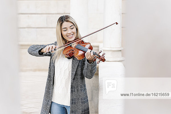 Blond young woman playing violin in city