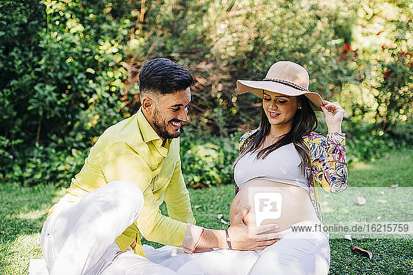 Glücklicher Mann  der den Bauch einer schwangeren Frau berührt  während er im Park sitzt