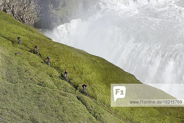 Island  Männer beim Mountainbiking neben einem Wasserfall