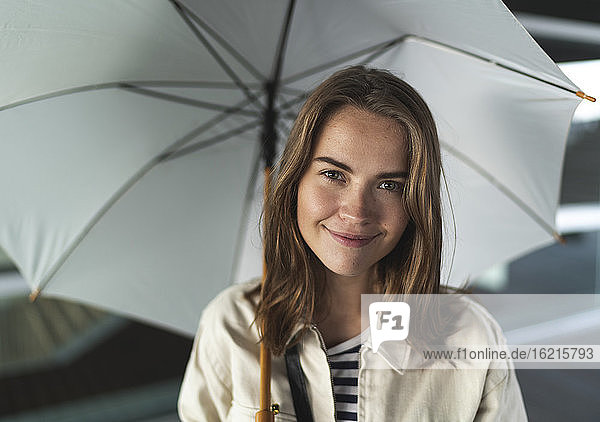 Nahaufnahme einer glücklichen jungen Frau mit Regenschirm in der Stadt stehend