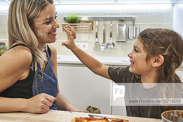 Verspieltes Mädchen beschmutzt die Nase der Mutter mit Soße in der Küche