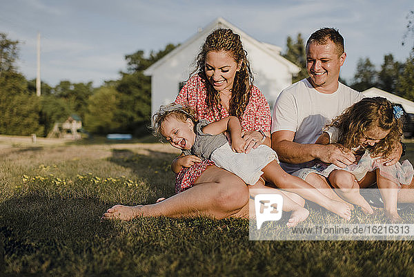 Glückliche Eltern mit zwei Töchtern sitzen auf einer Wiese vor ihrem Haus