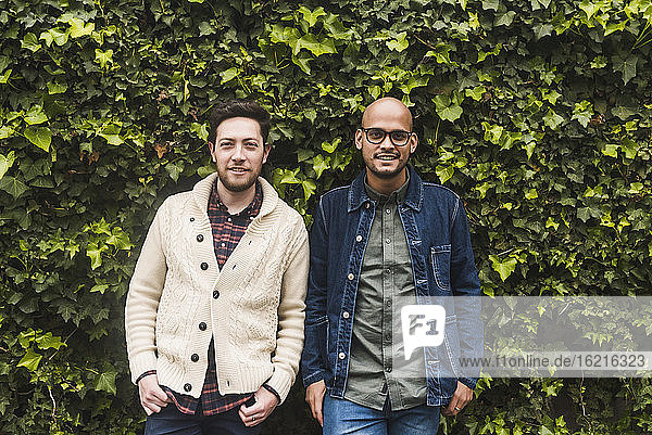 Gay couple standing against plants in park