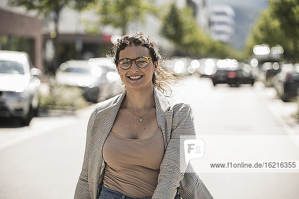 Lächelnde junge Frau mit Brille auf der Straße in der Stadt