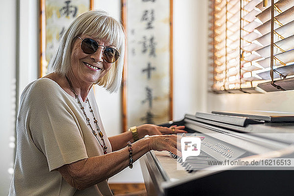 Happy senior woman wearing sunglasses playing piano at home