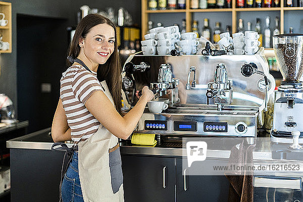 Glückliche weibliche Barista mit Kaffeemaschine im Café