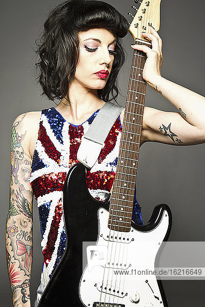 Junge Frau mit Gitarre und Tattoo auf ihrer Hand vor grauem Hintergrund