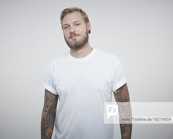 Portrait of young man with tattoos against white background