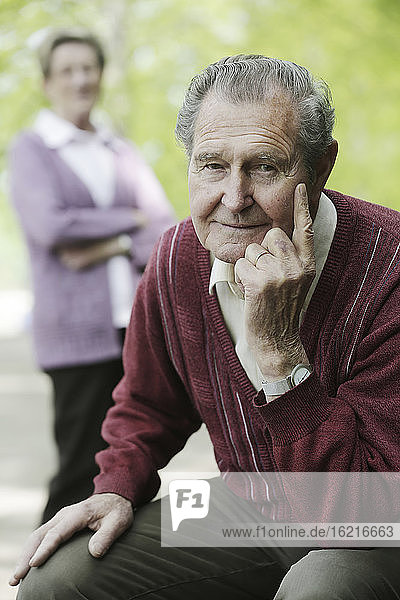 Deutschland  Köln  Porträt eines älteren Mannes im Park  während eine Frau im Hintergrund steht