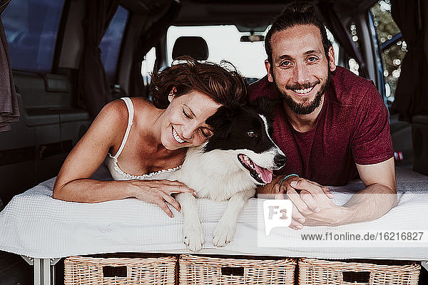 Smiling couple with dog lying in motor home