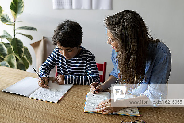 Junge Frau sitzt mit Schülerin bei den Hausaufgaben auf dem Tisch zu Hause