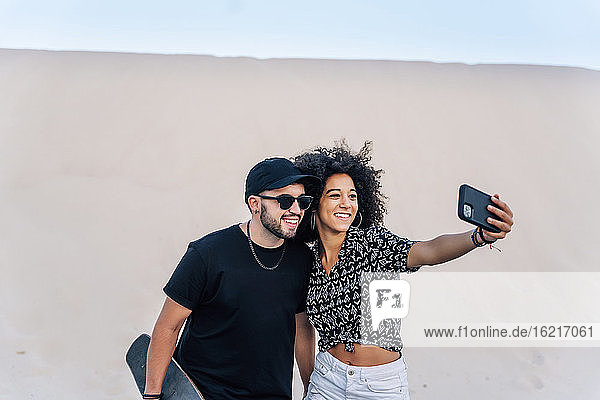 Couple taking selfie while standing against sand dune