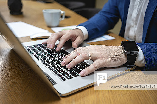 Close-up of businessman typing while using laptop at desk in creative coworking space