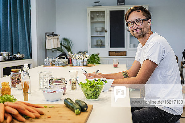 Lächelnder männlicher Student  der an einer Kücheninsel in einer Kochschule sitzt