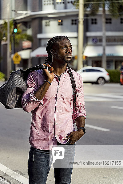 Thoughtful afro young man with bag standing on street in Miami  Florida  USA