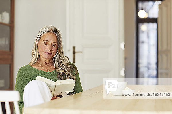 Frau liest ein Buch  während sie zu Hause am Tisch sitzt