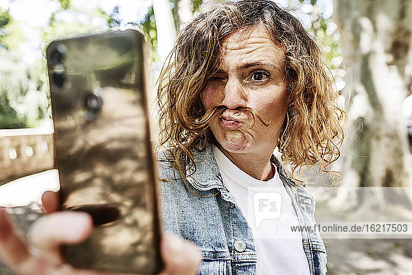 Nahaufnahme einer Frau  die ein Gesicht macht  während sie ein Selfie mit ihrem Smartphone im Park macht