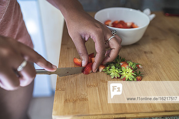 Close-up of young woman chopping strawberries on cutting board in kitchen at home