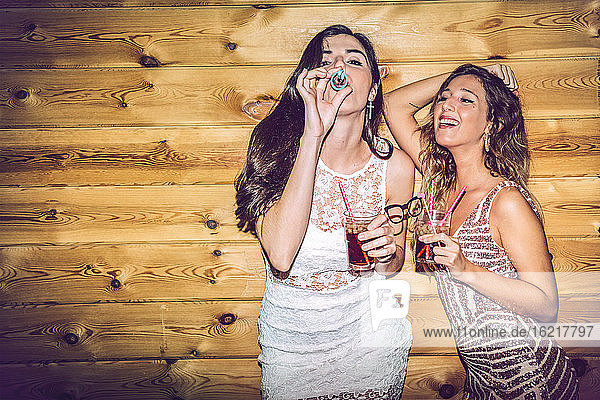 Betrunkene Freundinnen mit Requisiten und Getränken  die auf einer Party an der Wand stehen