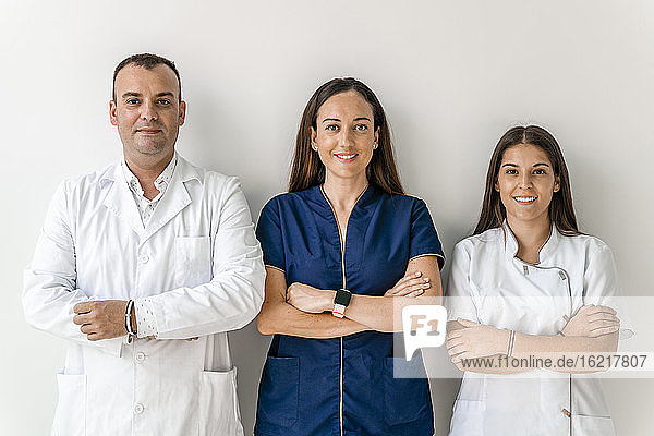 Lächelnde Ärzte mit vor der Wand verschränkten Armen in einer Zahnklinik