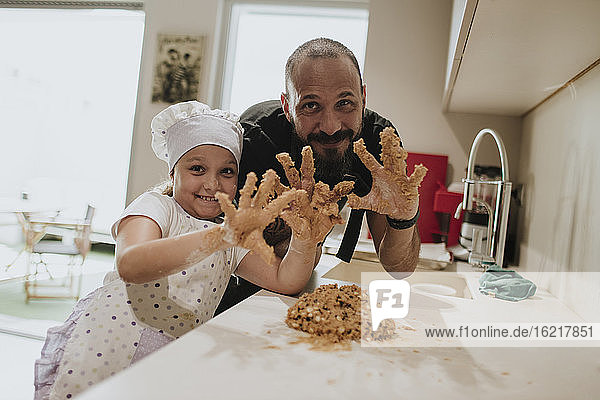 Vater und Tochter backen zu Hause Kekse und zeigen ihre Hände mit Teig