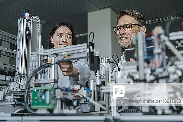Smiling male and female engineers examining equipment in laboratory