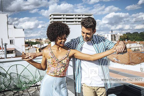 Multi-ethnisches Paar tanzt auf der Penthouse-Terrasse an einem sonnigen Tag