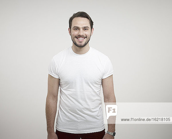Portrait of young man standing against white background  smiling