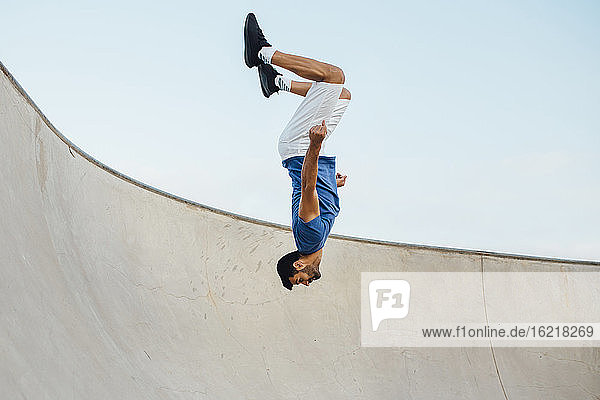 Upside down junger Mann macht Wallflip auf Sport-Rampe gegen Himmel