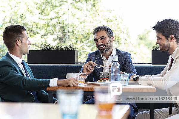 Lächelnder Geschäftsmann diskutiert mit Mitarbeitern während eines Treffens im Café