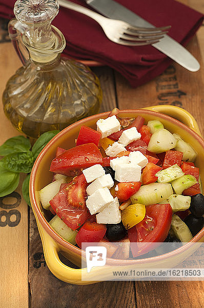 Schüssel mit griechischem Salat mit Fetakäse und schwarzen Oliven auf Holztisch  Nahaufnahme