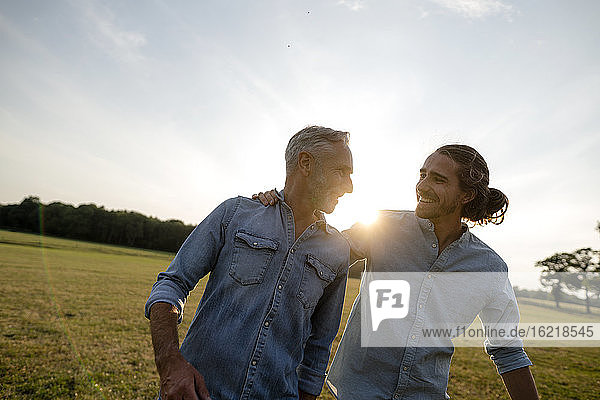 Glücklicher Vater mit erwachsenem Sohn auf einer Wiese auf dem Lande bei Sonnenuntergang