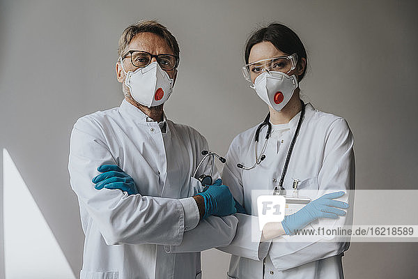 Ärzte mit Masken und verschränkten Armen stehen an einer Wand im Krankenhaus
