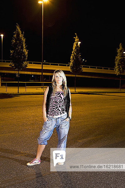 Deutschland  Köln  Junge Frau auf Parkplatz stehend  Hände in der Tasche  Portrait