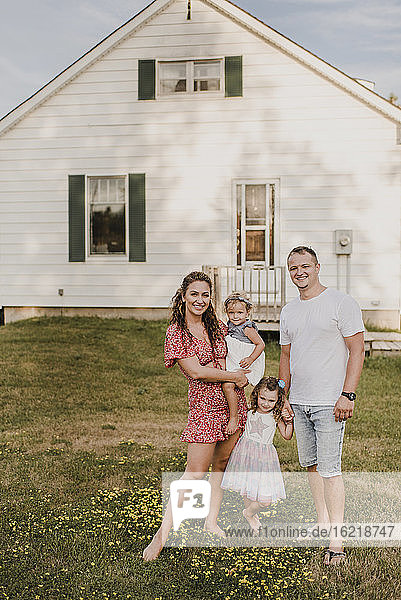 Porträt von lächelnden Eltern mit zwei Töchtern vor ihrem Haus