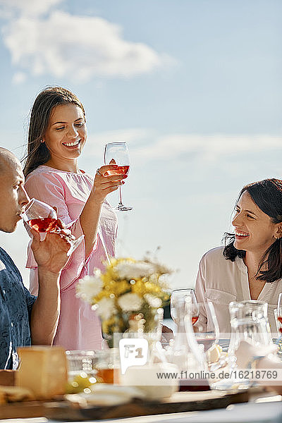 Junge Frau isst mit Freunden zu Abend und hebt ein Weinglas