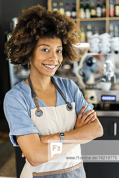 Confident female barista standing arms crossed in cafe