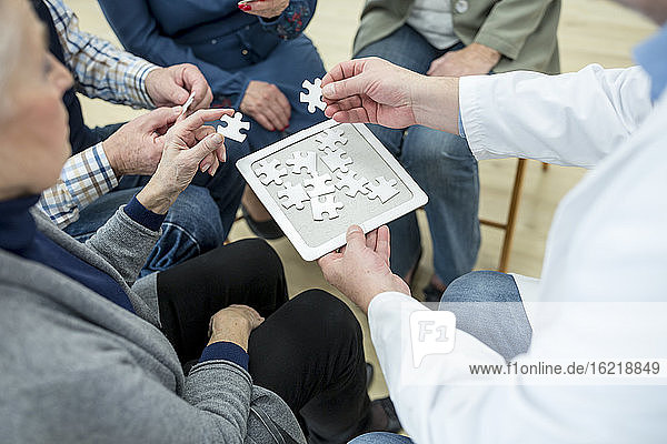 Arzt spielt Puzzle mit einer Gruppe von Senioren im Altersheim