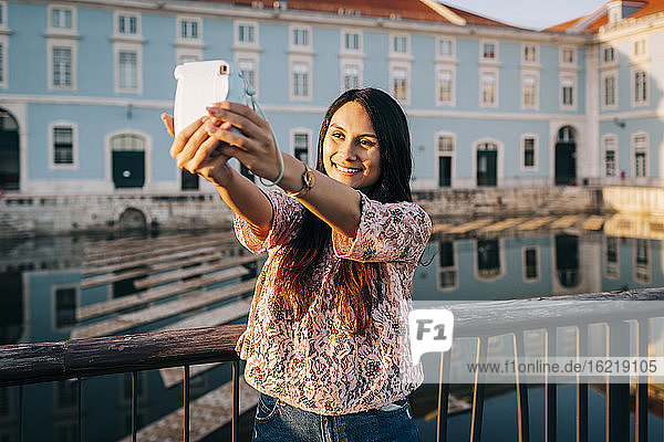 Junge Frau  die ein Selfie durch die Kamera macht  während sie auf einer Brücke steht